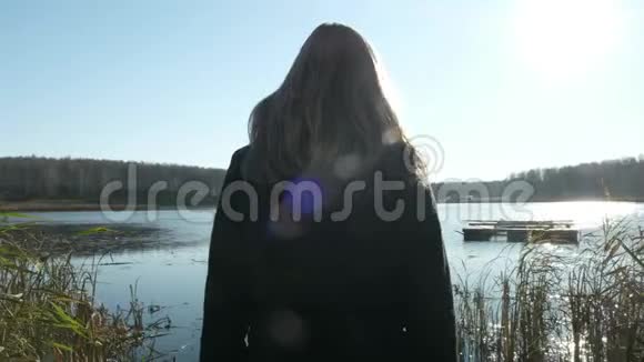 一个穿外套的漂亮金发女孩正走在湖边的码头上在湖面上秋天和多云的心情视频的预览图
