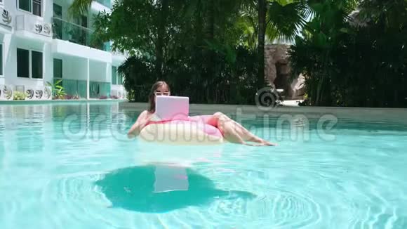 女孩在游泳池里的充气圈里带着笔记本电脑自由职业和娱乐的概念视频的预览图