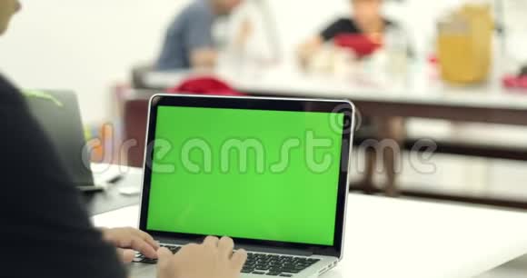 一名亚裔男子用绿色钥匙屏幕在笔记本电脑上打字的肩膀上的镜头视频的预览图