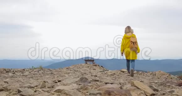 徒步旅行的女人穿着黄色雨衣背着背包在山里散步视频的预览图