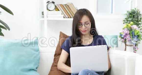 戴眼镜的年轻女人坐在沙发上在家里用笔记本电脑视频的预览图