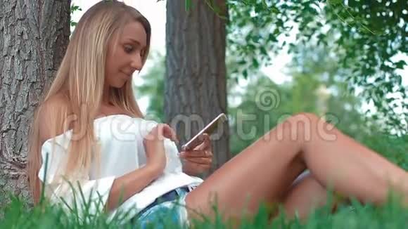 微笑的年轻女子触摸手机躺在草地上视频的预览图