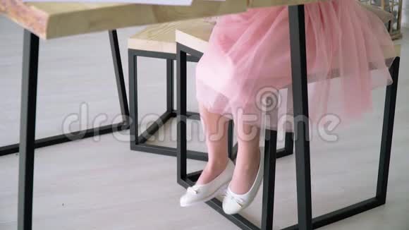 一个穿着粉红色裙子和白色鞋子的小女孩坐在桌子旁视频的预览图
