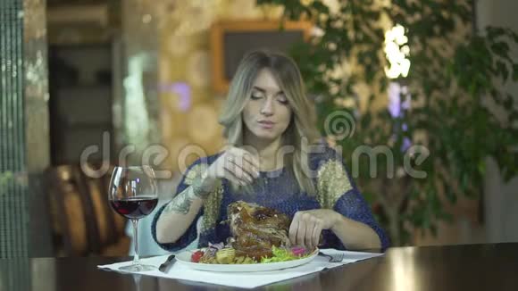 年轻的纹身漂亮的金发女孩在高档餐厅撕肉用手指吃不当行为视频的预览图