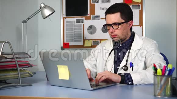 一位带听诊器的治疗师在他的办公室里用笔记本电脑治疗病人视频的预览图