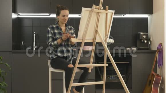 女艺术家在画布上绘画使用丙烯酸涂料坐在酒吧椅子上在现代厨房女性用画笔绘制图片我是视频的预览图