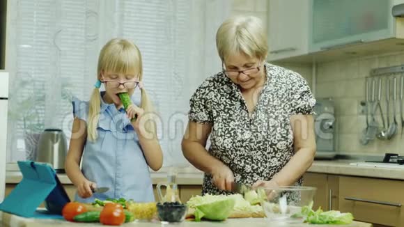 有趣的女孩6岁帮助她的祖母在厨房准备食物吃黄瓜一起玩健康视频的预览图
