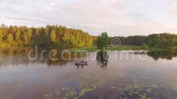 橡皮船上的两个渔夫和白天鹅一起漂浮无人机空中射击朋友们在阳光明媚的森林里的湖边小船上放松视频的预览图