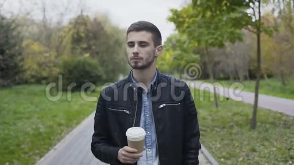 帅哥走在秋天公园的小巷里喝咖啡视频的预览图