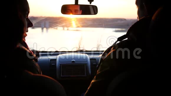 年轻的男女正坐在前排座位的车里在一片红日落下转身挥手致意视频的预览图