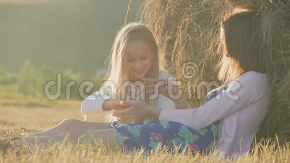 妈妈和女儿在日落时坐在稻草堆上母亲和她的小女儿在户外野外玩得很开心这就是视频的预览图