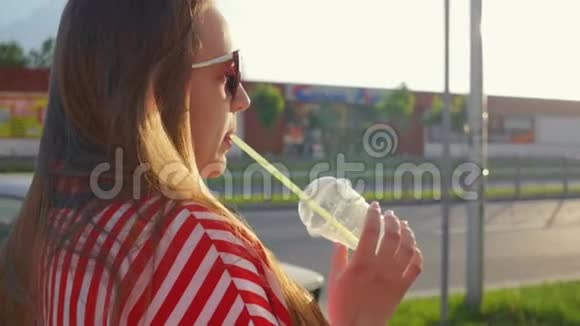 夏天穿红色衣服的年轻快乐女孩的肖像女孩从稻草中喝酒近距离射击视频的预览图