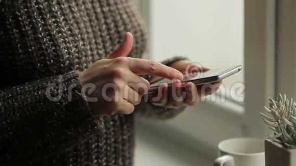 一个女人站在房间里的窗户附近使用手机视频的预览图