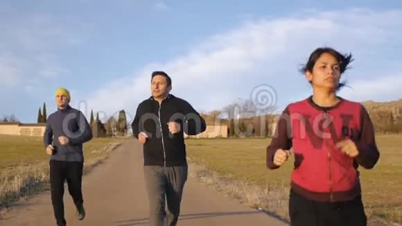 与户外私人教练一起健身两个男人和女人在秋天缓慢地沿着乡间小路跑视频的预览图