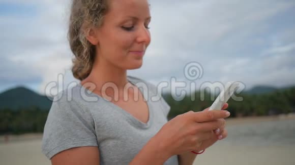 桑迪海滩上有卷发的年轻快乐女孩用手机发短信高清慢速运动泰国视频的预览图