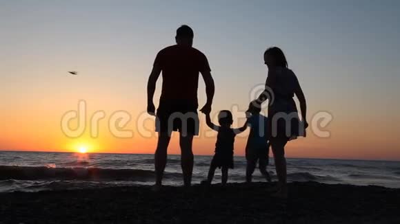 日落时海边的家庭剪影爸爸妈妈孩子们视频的预览图