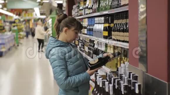 超市里的女人年轻的白种人女士穿着蓝色夹克在商店的货架背景上选择起泡葡萄酒视频的预览图
