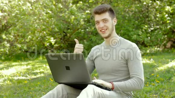 在公园拿着笔记本电脑工作的年轻人竖起大拇指视频的预览图