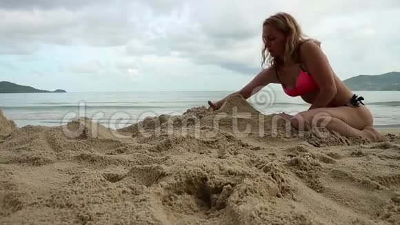 美丽苗条的女人在异国海滩玩沙视频的预览图