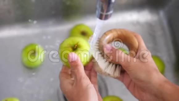 年轻的纯素女孩用竹刷洗绿苹果手拿着新鲜水果在厨房水槽的流水下视频的预览图