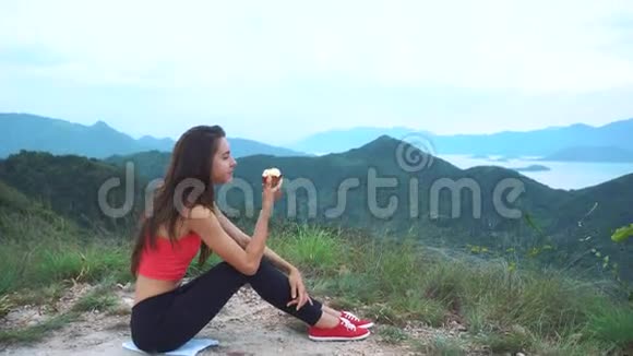 运动的女人在山上锻炼后吃红苹果鸟瞰令人惊叹的美丽山脉小岛屿国家视频的预览图