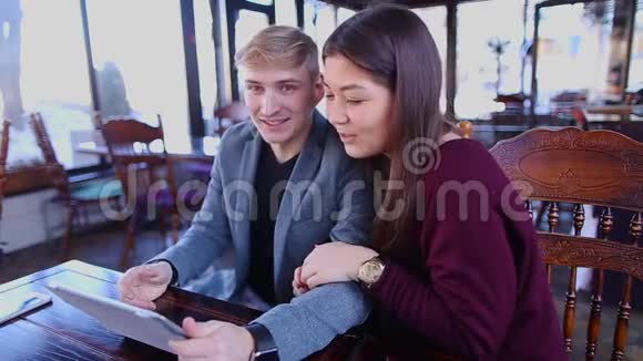 男孩和女孩坐在咖啡桌上拿着平板电脑笑着视频的预览图