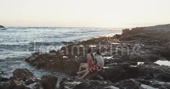 日落时两个孩子坐在沙滩上视频的预览图