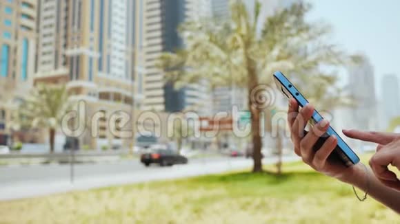 在迪拜的城市街道背景下女孩在智能手机上拨打一个号码或信息双手特写视频的预览图