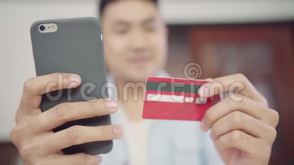 亚裔男子使用智能手机进行网上购物和信用卡在互联网上的客厅家视频的预览图
