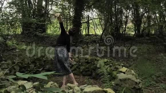 4K美丽的女孩穿着黑色手工制作的裙子在一片绿色的森林中在一个小的大石头上跳舞视频的预览图