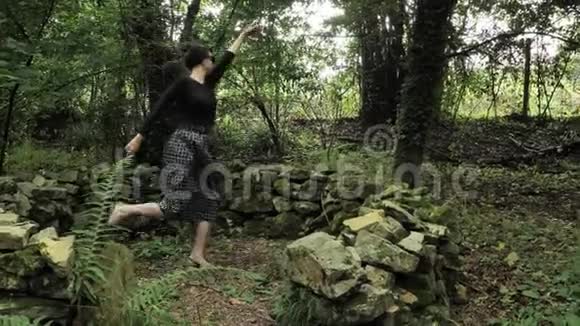 4K美丽的女孩穿着黑色手工制作的裙子在一片绿色的森林中在一个小的大石头上跳舞视频的预览图
