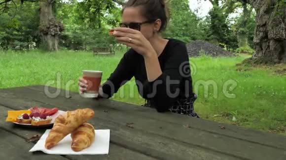 在橡树林的木桌上穿着黑色手工衣服的漂亮女孩吃着美味的饭菜视频的预览图