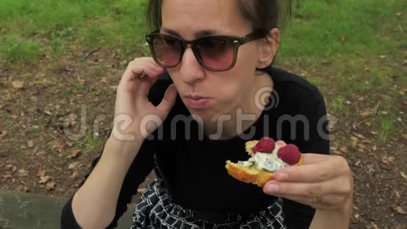 在橡树林的木桌上穿着黑色手工衣服的漂亮女孩吃着美味的饭菜视频的预览图