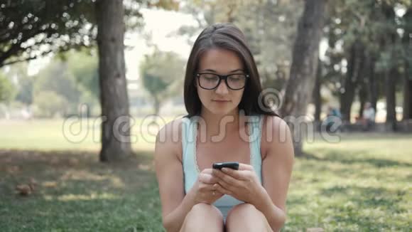 利用电话网上购物理念特写公园草坪上年轻美女的肖像视频的预览图