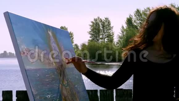 夏天河边海滩上日出时一位美丽的女艺术家手里拿着画笔画了一幅画她是个女人视频的预览图