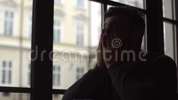 年轻人坐在靠近窗户的咖啡馆里向远处望去他愁眉苦脸心情不好双手握在前面视频的预览图