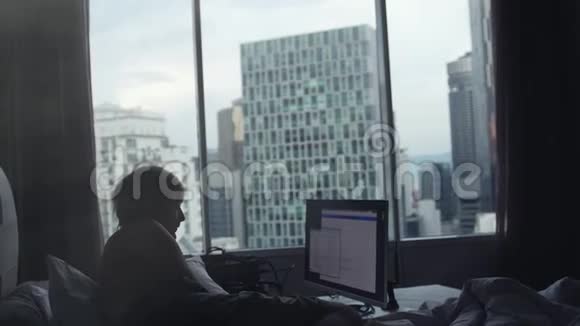 年轻的商人正在做笔记本电脑躺在床边的窗户上在背景上建筑3840x2160视频的预览图