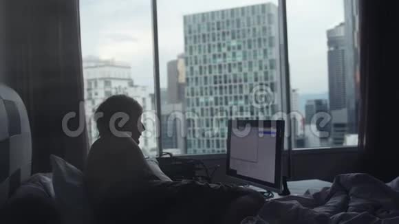 年轻的商人正在做笔记本电脑躺在床边的窗户上在背景上建筑3840x21604k视频的预览图