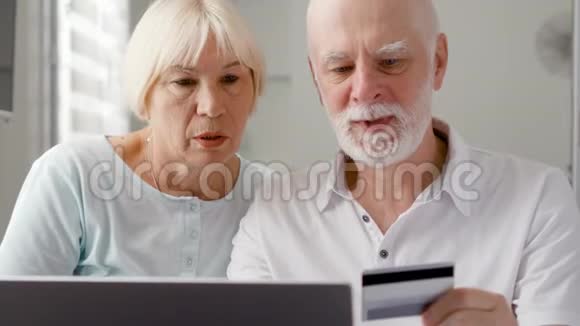 家里的老夫妇用笔记本电脑上的信用卡在线购物退休后积极的现代生活视频的预览图