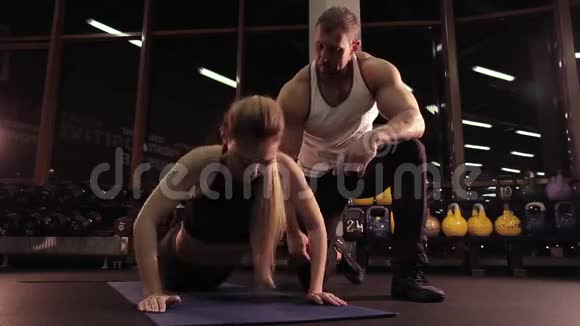 在健身俱乐部锻炼的年轻有魅力的女人她的健身教练看上去视频的预览图