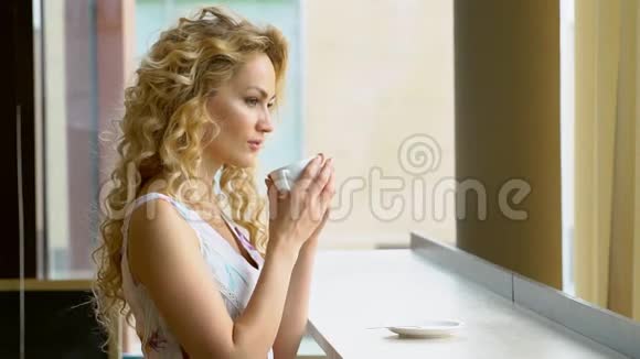 美丽的金发女孩在咖啡馆喝一杯热咖啡或茶视频的预览图