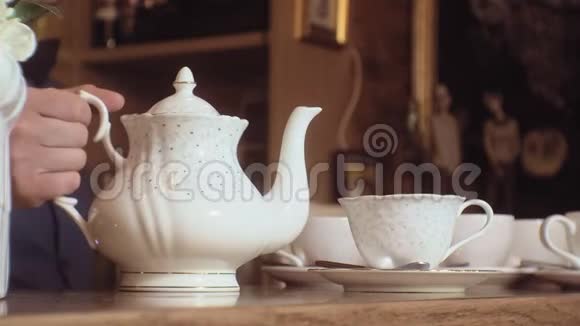 一个人把茶从水壶里倒进木桌上的白色杯子里视频的预览图
