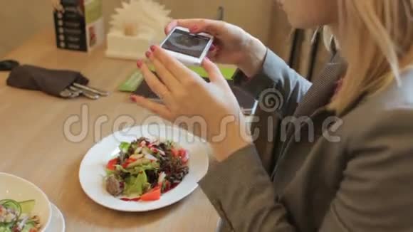 年轻的金发女郎在餐厅用智能手机拍下美味沙拉视频的预览图