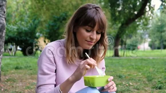 一个年轻漂亮的女孩吃素食沙拉的肖像女学生在公园吃午饭重量损失视频的预览图
