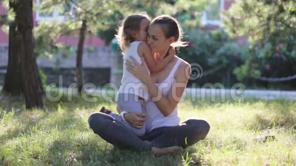 在绿色公园做瑜伽运动时母亲和女儿坐在一起拥抱视频的预览图