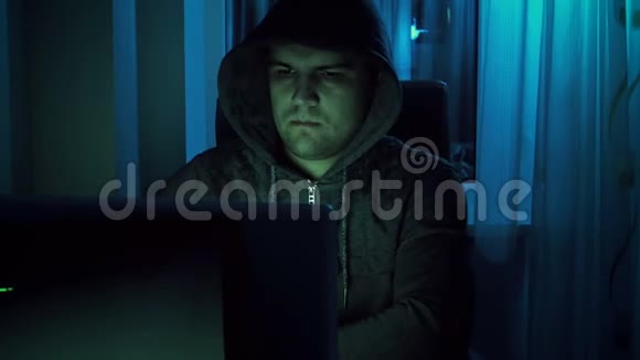 穿着连帽衫的年轻男性黑客夜间在家中用笔记本电脑工作的4k镜头视频的预览图