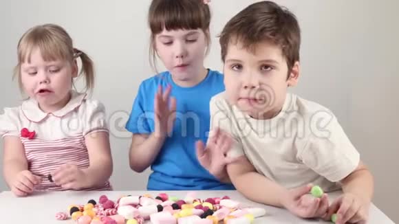 三个快乐的孩子吃糖果坐在桌子旁视频的预览图
