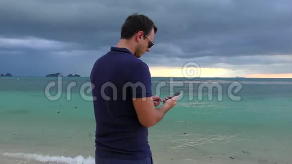 在多云的黑暗天气里一个人在海滩上用智能手机说话视频的预览图
