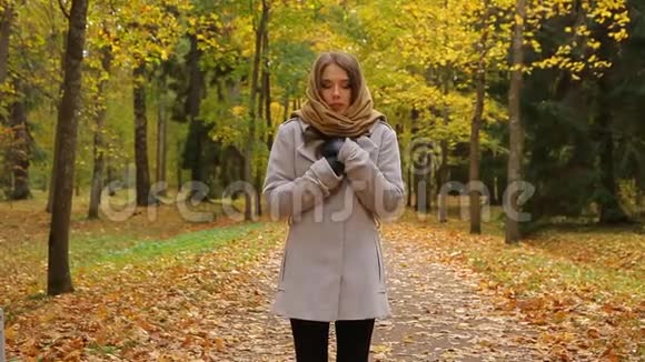 一位迷人的年轻女子站在秋天的公园里因寒冷而战栗视频的预览图