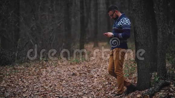 戴眼镜的人正穿过秋天的森林使用智能手机慢动作视频的预览图